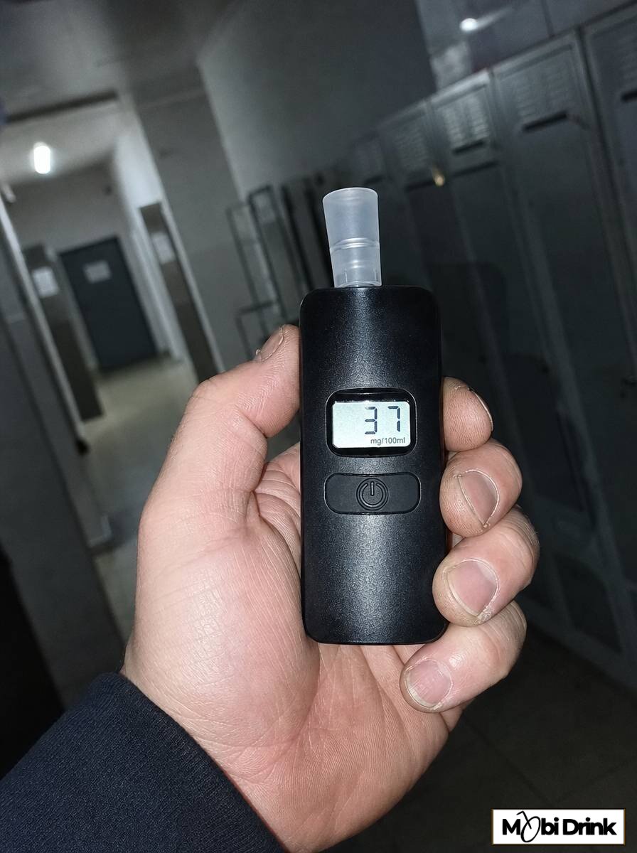 Wyświetlacz alkomatu z wynikiem pomiaru w dłoni pracownika w zakładzie pracy