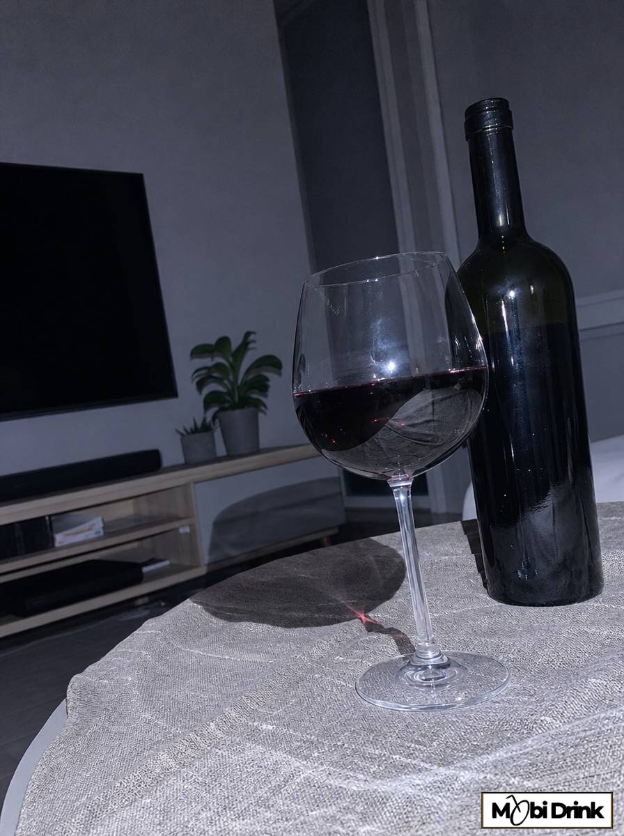 Kieliszek czerwonego wina 150 ml obok butelki na stole w salonie wieczorem
